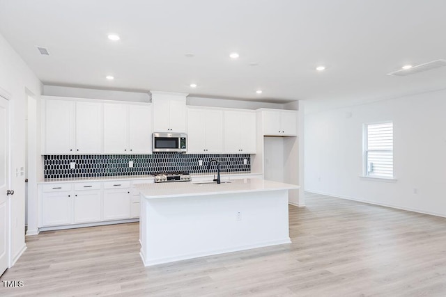 kitchen with white cabinetry, an island with sink, stove, and backsplash