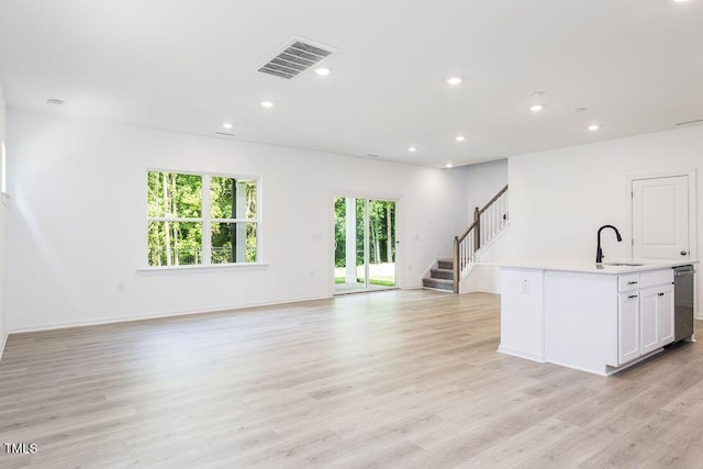 kitchen featuring sink, light hardwood / wood-style flooring, dishwasher, white cabinets, and a center island with sink