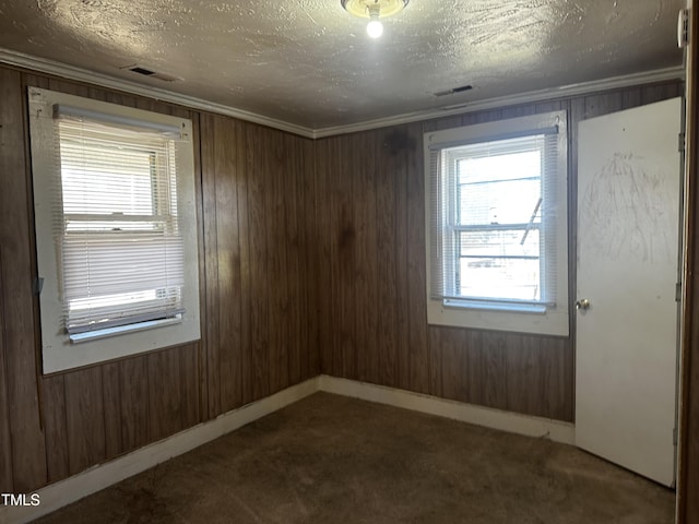 empty room featuring crown molding, wooden walls, a textured ceiling, and carpet flooring