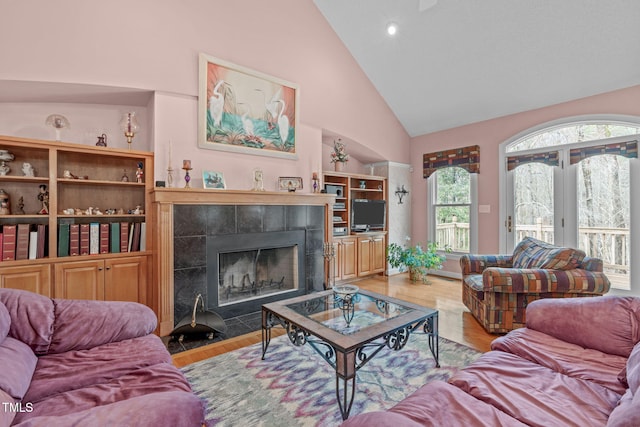 living room featuring high vaulted ceiling, light hardwood / wood-style floors, and a tile fireplace