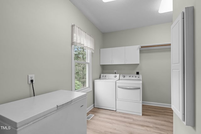 washroom with washing machine and dryer, cabinets, a textured ceiling, and light wood-type flooring