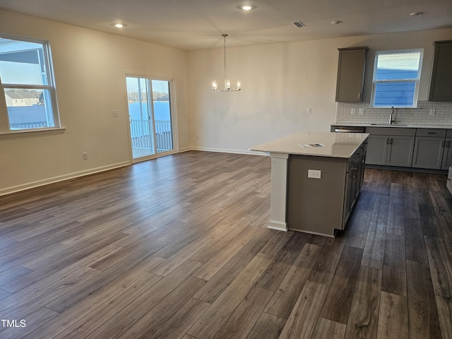 kitchen with gray cabinetry, tasteful backsplash, decorative light fixtures, a center island, and dark hardwood / wood-style flooring