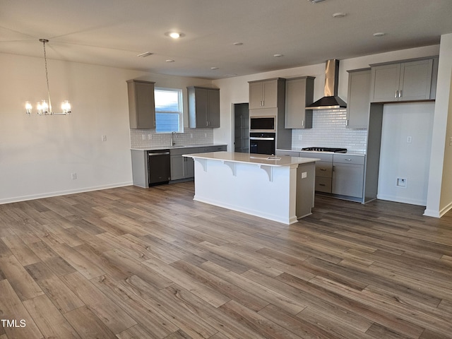 kitchen with gray cabinetry, wall chimney range hood, black appliances, and a kitchen island