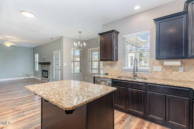 kitchen featuring sink, light hardwood / wood-style flooring, a stone fireplace, a center island, and decorative light fixtures