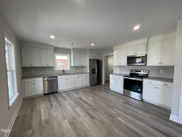 kitchen featuring sink, light hardwood / wood-style flooring, appliances with stainless steel finishes, white cabinetry, and light stone countertops