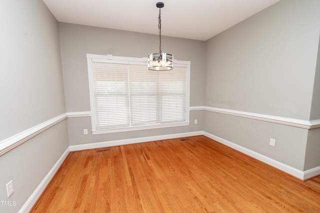 spare room featuring hardwood / wood-style flooring and a chandelier