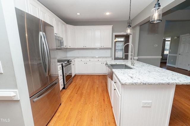 kitchen featuring pendant lighting, white cabinets, stainless steel appliances, a center island with sink, and light hardwood / wood-style flooring