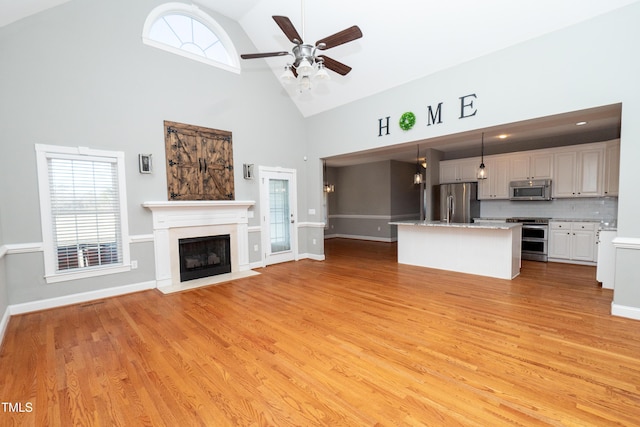 unfurnished living room with ceiling fan, high vaulted ceiling, and light hardwood / wood-style floors