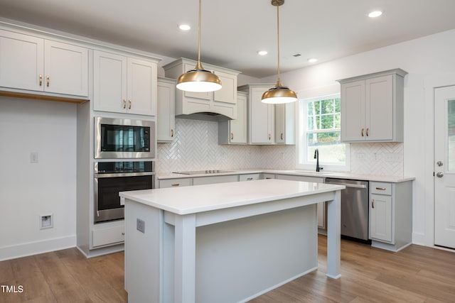 kitchen featuring light wood-style flooring, a kitchen island, light countertops, appliances with stainless steel finishes, and pendant lighting