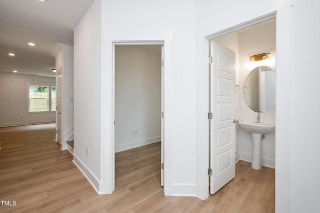 corridor with light wood finished floors, recessed lighting, a sink, and baseboards