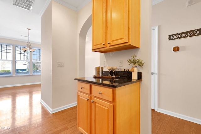 kitchen featuring crown molding, hanging light fixtures, light hardwood / wood-style flooring, a notable chandelier, and dark stone counters