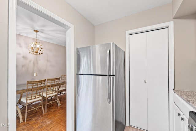 kitchen with a chandelier, hanging light fixtures, stainless steel fridge, light parquet floors, and white cabinets