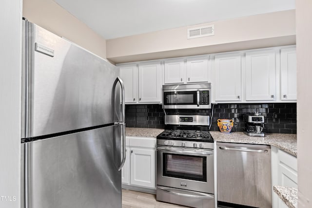 kitchen featuring light hardwood / wood-style flooring, appliances with stainless steel finishes, white cabinetry, light stone counters, and tasteful backsplash