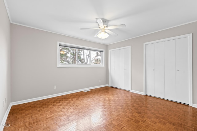 unfurnished bedroom with parquet floors, crown molding, and two closets