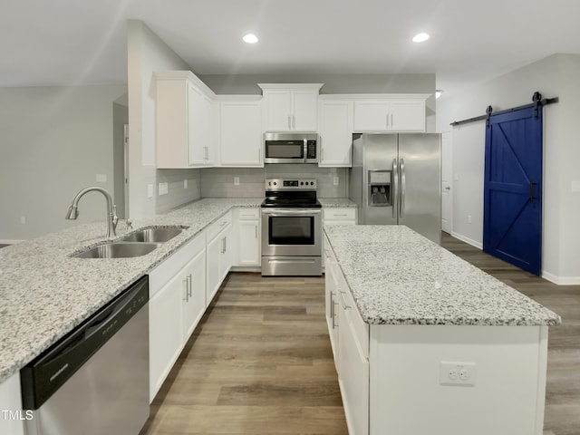 kitchen featuring light stone counters, appliances with stainless steel finishes, a barn door, and sink