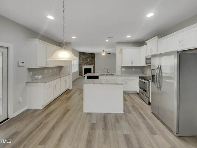 kitchen featuring pendant lighting, sink, appliances with stainless steel finishes, light stone counters, and white cabinets