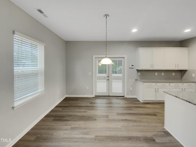 kitchen with light stone counters, tasteful backsplash, decorative light fixtures, hardwood / wood-style flooring, and white cabinets