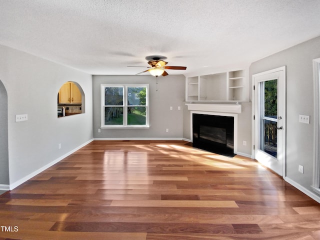 unfurnished living room with hardwood / wood-style flooring, a large fireplace, ceiling fan, and a textured ceiling