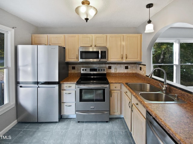 kitchen with light tile patterned flooring, light brown cabinetry, sink, hanging light fixtures, and appliances with stainless steel finishes