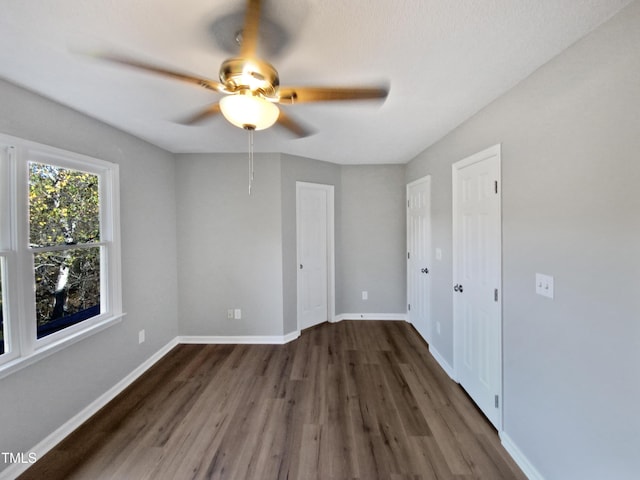 unfurnished bedroom featuring ceiling fan, dark hardwood / wood-style flooring, and two closets