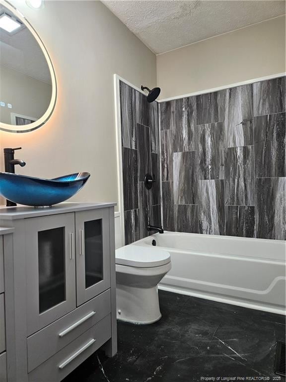 full bathroom with vanity, tiled shower / bath combo, toilet, and a textured ceiling