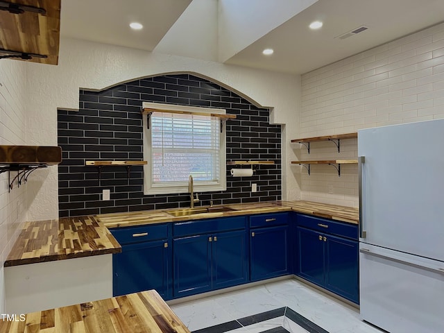 kitchen with blue cabinets, sink, wooden counters, decorative backsplash, and white fridge