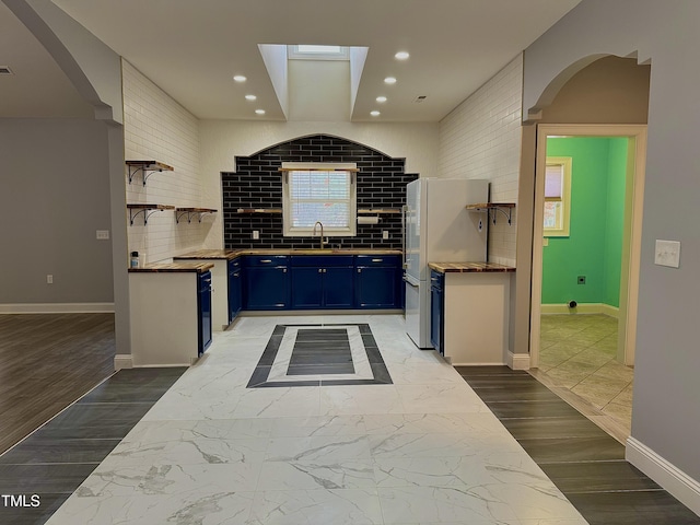 kitchen featuring blue cabinets, sink, white refrigerator, hardwood / wood-style floors, and backsplash