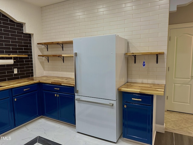 kitchen featuring blue cabinetry, wooden counters, and refrigerator