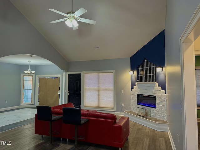 living room with a fireplace, ceiling fan with notable chandelier, dark wood-type flooring, and high vaulted ceiling