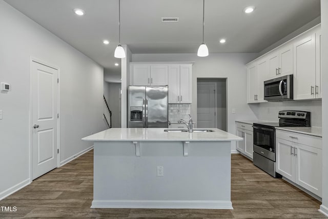 kitchen featuring stainless steel appliances, white cabinetry, pendant lighting, and an island with sink