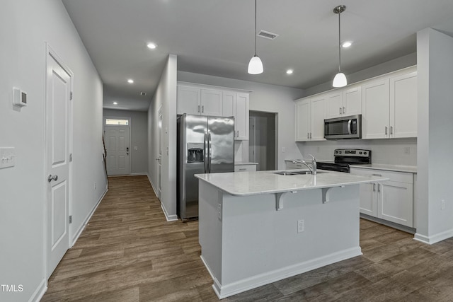 kitchen with appliances with stainless steel finishes, white cabinetry, sink, hanging light fixtures, and a center island with sink