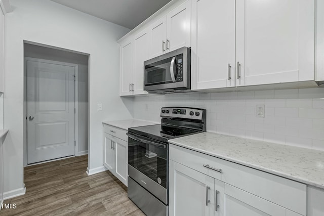 kitchen featuring white cabinetry, wood-type flooring, stainless steel appliances, light stone countertops, and backsplash