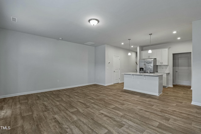 kitchen with white cabinetry, wood-type flooring, stainless steel fridge with ice dispenser, hanging light fixtures, and a kitchen island with sink