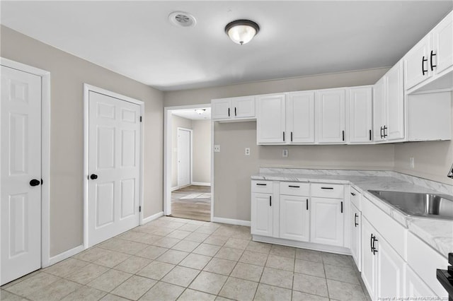 kitchen featuring light tile patterned flooring, light stone countertops, sink, and white cabinets