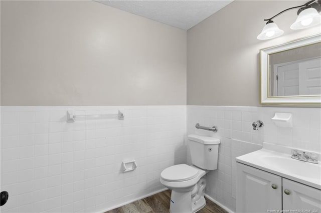 bathroom with tile walls, hardwood / wood-style flooring, vanity, toilet, and a textured ceiling