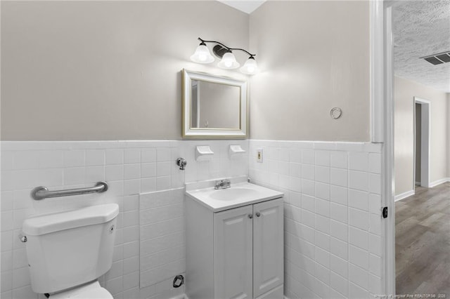 bathroom featuring hardwood / wood-style flooring, tile walls, vanity, a textured ceiling, and toilet