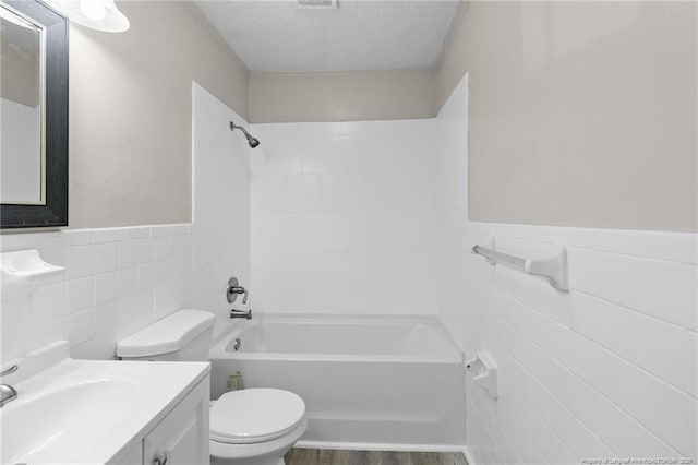 full bathroom featuring tile walls, tiled shower / bath combo, vanity, a textured ceiling, and toilet