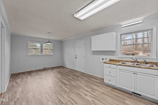 kitchen with pendant lighting, white cabinetry, sink, crown molding, and light hardwood / wood-style flooring