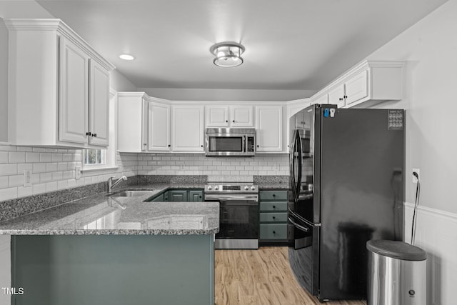 kitchen with sink, white cabinetry, dark stone countertops, kitchen peninsula, and stainless steel appliances