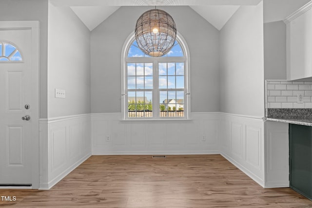 unfurnished dining area with lofted ceiling, light hardwood / wood-style floors, and a notable chandelier