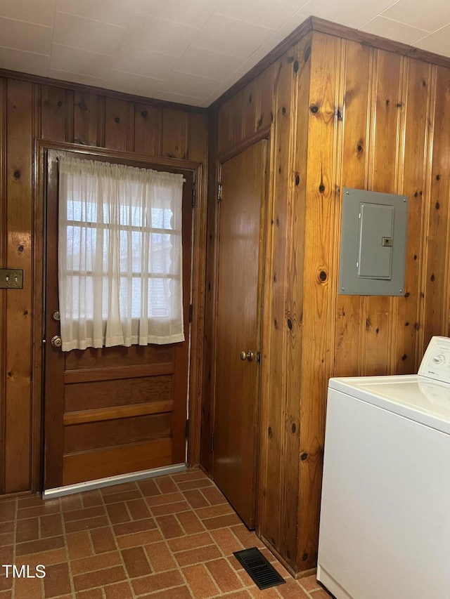 laundry room with electric panel, washer / dryer, and wood walls