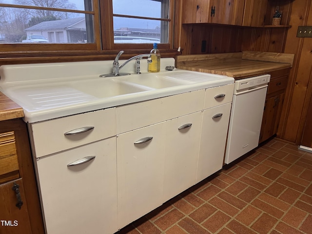 kitchen with white dishwasher, sink, white cabinets, and wood walls