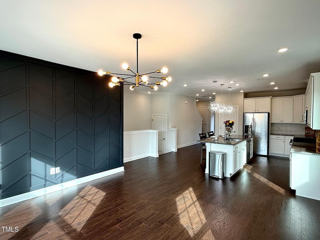 kitchen featuring white cabinetry, decorative light fixtures, stainless steel appliances, and a center island with sink