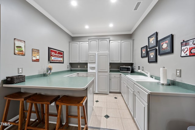 kitchen featuring gray cabinets, a breakfast bar area, ornamental molding, light tile patterned floors, and kitchen peninsula