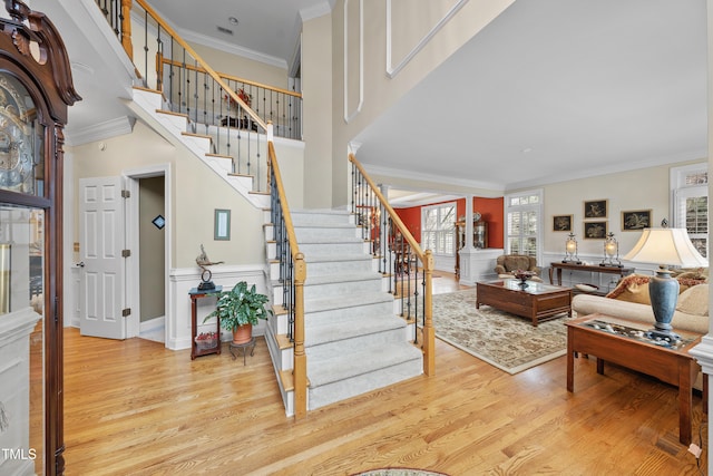 foyer entrance with a high ceiling, ornamental molding, and light wood-type flooring