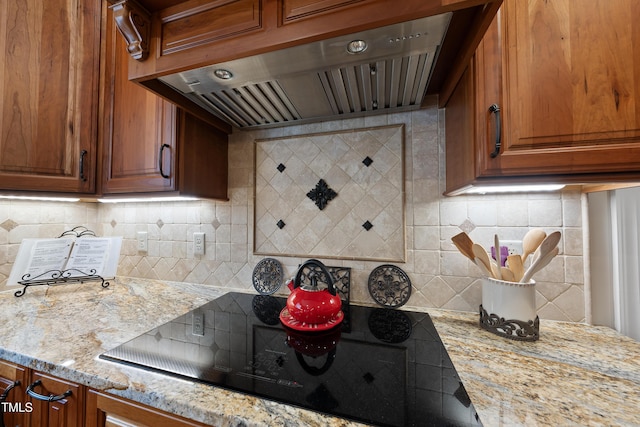 kitchen featuring black electric stovetop, wall chimney exhaust hood, light stone countertops, and backsplash