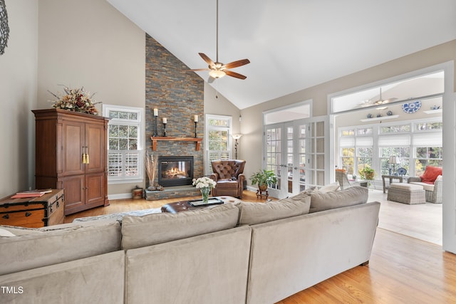 living room featuring high vaulted ceiling, a wealth of natural light, a stone fireplace, and light hardwood / wood-style floors