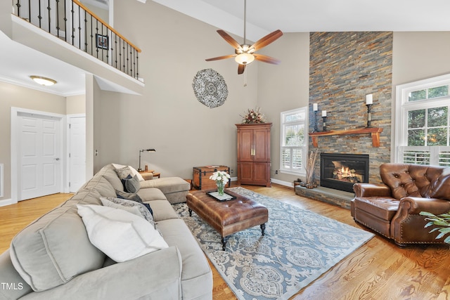 living room with crown molding, ceiling fan, high vaulted ceiling, a stone fireplace, and light wood-type flooring