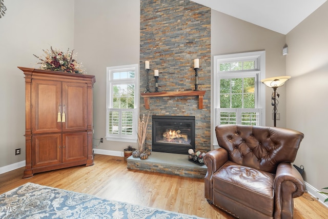 living area with a fireplace, high vaulted ceiling, and light wood-type flooring