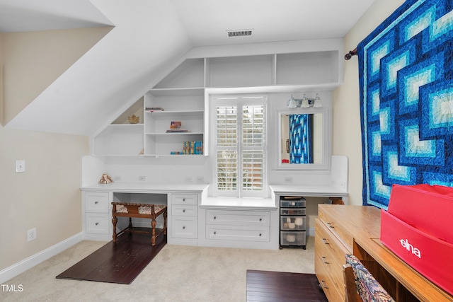 home office with light colored carpet, built in desk, and vaulted ceiling